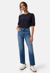 Maglietta blu navy a maniche corte con tessuto a trama e dettagli scintillanti, abbinata a jeans blu a vita alta e sneakers bianche.