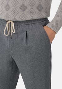 Pantalons de survêtement en tricot gris avec une taille à cordon de serrage, en tissu texturé de couleur claire et avec des poches latérales.