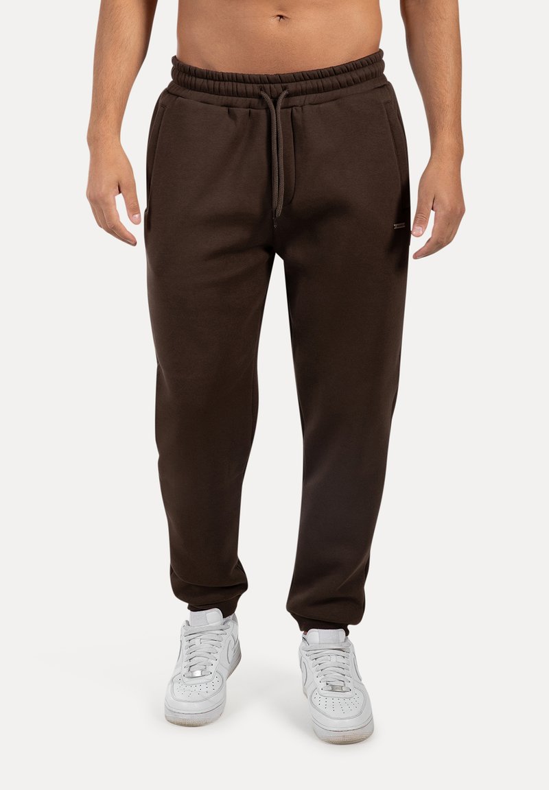 Brune sweatpants lavet af blødt stof med elastisk talje, snøre og sidelommer. Bæres med hvide sneakers.