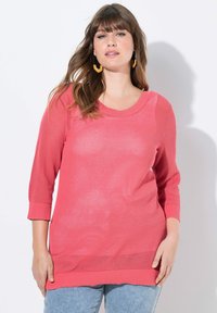 Suéter de punto ligero en color coral con un patrón texturizado, mangas 3/4 y un escote ancho, combinado con unos jeans de mezclilla azules.