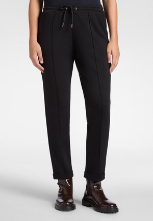 Schwarze schmal zulaufende Hose mit einem Kordelzugbund, subtilen Seitennähten und umgeschlagenen Säumen, kombiniert mit braunen Knöchelstiefeln. Glatte Stofftextur.