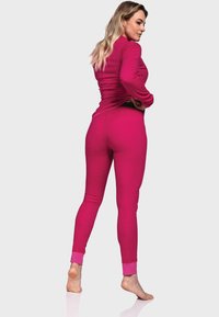 Enganliegendes, langärmliges Oberteil und Leggings aus leuchtend pinkem Stoff. Auffällige Details sind der kontrastierende Saum am Knöchel. Glatte Textur.