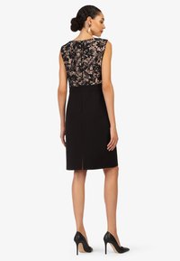 Robes noires avec un dos en dentelle, design sans manches, longueur de genou et fente sur le côté, associée à des escarpins noirs.