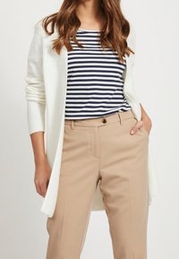 Vit kavaj över en marinblå och vit randig skjorta, i kombination med beiga skräddarsydda byxor. Klädseln har texturerat tyg och en avslappnad passform.