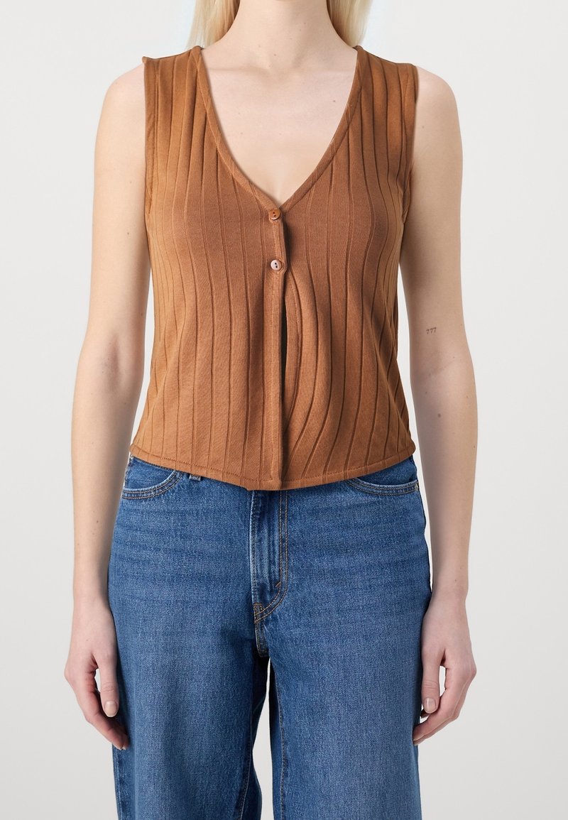Brązowy, prążkowany top bez rękawów z głębokim dekoltem w kształcie litery V, z zapięciem na guziki z przodu. Połączony z niebieskimi dżinsami z wysokim stanem.