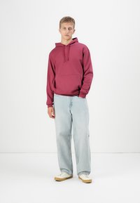 Maroon hoodie with a kangaroo pocket, paired with light blue baggy jeans and white sneakers with beige accents. Simple, relaxed design.