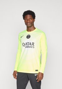 Garais piedurkņu, spilgti neona zaļais sporta krekls ar baltu centrālo logo, izbalējušām svītrām un melniem akcentiem. Izgatavots no viegla, elpojoša auduma.