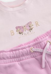 Ljusrosa bomullströja med fjärils grafik och guldtext. Kombinerad med mörkare rosa shorts med elastisk midja och snörning.