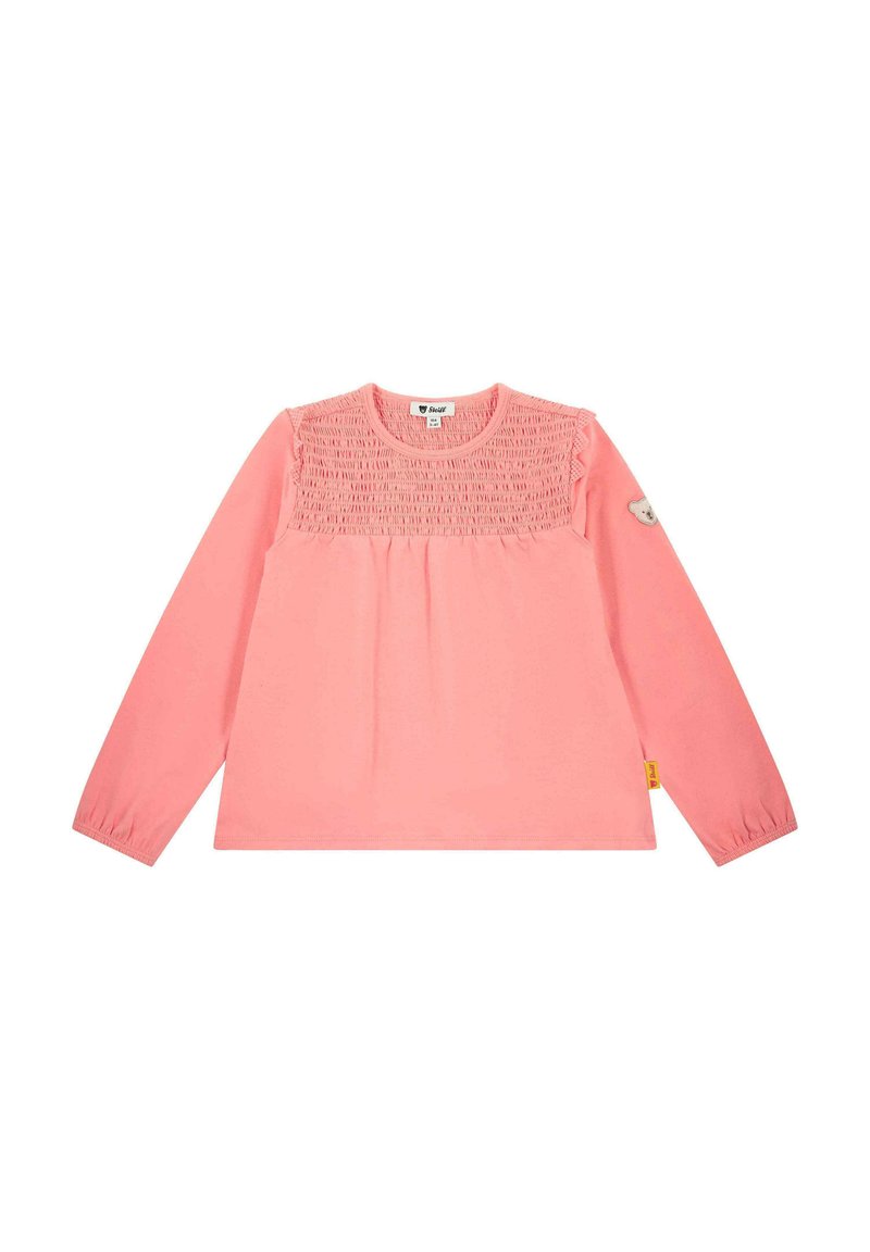 Lange mouwen roze shirt met geplooide smockdetails op de schouders, ronde halslijn en een kleine berenbadge op de linkermouw.