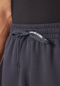 Navy sweatpants featuring an elastic waistband with a drawstring. Text is printed on the drawstring. Made from a soft, textured material.