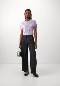 T-shirt à rayures violettes et blanches à manches courtes associé à un pantalon tailleur gris taille haute et des ballerines noires, tenant un petit sac en argent.