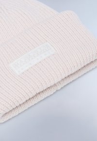 Berretto a maglia rosa chiaro con una trama a coste, dotato di un'etichetta bianca con logo in rilievo. Il polsino è leggermente ripiegato.