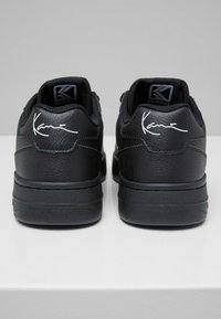 Schwarze Ledersneaker mit glatter Textur, gepolstertem Kragen und weißem Signature-Detail an der Ferse. Gummisohle mit subtiler Profilierung.