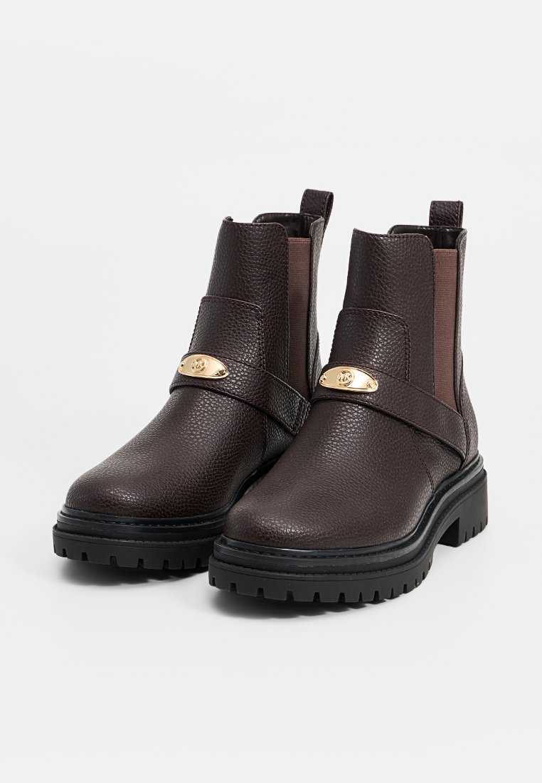 Botas de tobillo de cuero marrón con un acabado texturizado, paneles laterales elásticos, suela de goma y una correa de acento en tono dorado en la parte delantera.