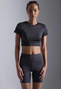 Sötét szürke sport crop top és magas derekú rövidnadrág sima, rugalmas anyagból. Minimalista dizájn, rövid ujjak és formás szabás.
