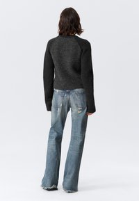 Donkergrijze gebreide trui met lange mouwen, gecombineerd met vervaagde blauwe flare jeans met beschadigingen en rafelige zoom.