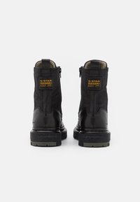 Botas negras hasta el tobillo con parte superior de cuero y textil, tacón reforzado, cierre de cremallera y suela de goma texturizada; presenta la marca G-Star en la parte posterior.