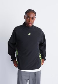 Black sweatshirt with a high collar, featuring a small green logo and striped accents in a bright green along the sides.