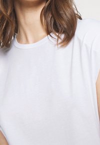 Bílý bavlněný tričko s kulatým výstřihem a krátkými rukávy, s volným střihem a hladkou texturou. Bez vzoru.