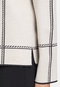 Light beige sweater with black grid pattern. Features a logo 'SCSY' in pale tone and a side slit, crafted from a soft knit fabric.