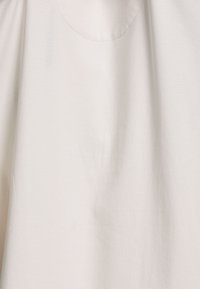 Hellebeige Baumwollstoff mit glatter Textur; verfügt über eine abgerundete Tasche und subtile Stichdetails, die ein minimalistisches Design schaffen.