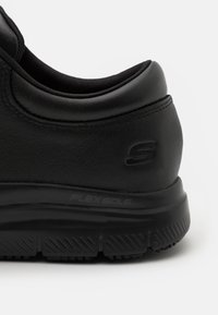 Svart sneaker med övre del i strukturerat läder, vadderad krage och en gummisula märkt "FLEX SOLE" med ett mönstrat däck för bra grepp.