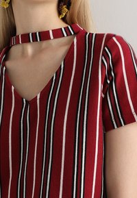 Top a rayas rojas y blancas con mangas cortas, que presenta un escote en V y un cuello abierto. Tejido texturizado con rayas horizontales y verticales.