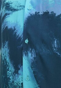 Primer plano de una tela azul con un patrón abstracto en azul oscuro y turquesa, y botones turquesa a juego cosidos en la prenda.