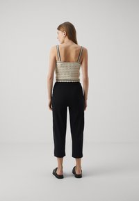 Top corto all'uncinetto di color crema con profili neri, abbinato a pantaloni neri a coste. Spalline sottili, vestibilità rilassata e design corto. Tessuto liscio.