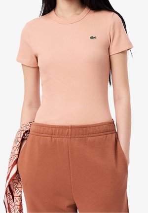 Jasnoróżowy prążkowany t-shirt z krótkim rękawem i okrągłym dekoltem oraz zielonym logo Lacoste. W połączeniu z brązowymi dresowymi spodenkami z bocznymi kieszeniami.