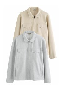 Dos chaquetas con cremallera: una de color beige claro con una textura suave y dos bolsillos en el pecho, y otra de color gris claro con una textura blanda y bolsillos en los laterales.