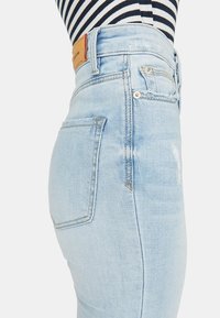 Jeans de mezclilla de talle alto en azul claro con una silueta ajustada, que cuentan con bolsillos traseros y un parche de cuero en la cinturilla.