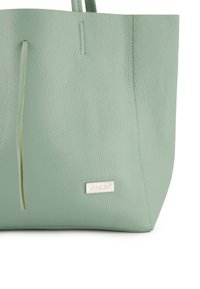 Mintgroene leren totebag met een gestructureerde afwerking, voorzien van een dunne leren accent en een zilveren logoplaat aan de voorkant.