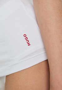 Biała koszula z krótkim rękawem z bawełny, z czerwonym logo "HUGO" po lewej stronie. Gładka faktura i luźny krój.