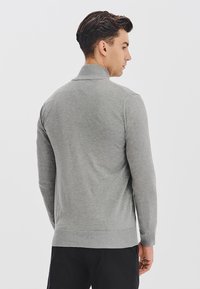 Szary sweter o miękkiej teksturze, długich rękawach i kołnierzu z wykładanym brzegiem. Projekt zawiera dopasowaną sylwetkę i prążkowany dół.