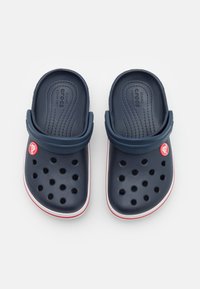 Pair of navy blue Crocs with red and white accents, ventilation holes, and adjustable heel straps on a plain white background.