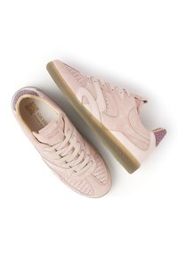 Ein Paar pinke Wildledersneaker mit Gummisohlen, Schnüren, durchbrochenen Details und gesprenkelten Fersenelementen, präsentiert vor weißem Hintergrund.