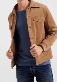 Brun kordflodeljacka med två bröstfickor, blå strukturstickad tröja under och mörk denimjeans. Slät tyg, knäppningar.