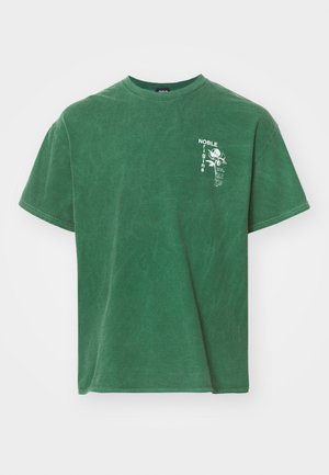 T-shirt en coton vert avec une coupe décontractée, présentant un imprimé graphique blanc sur la poitrine gauche. Manches courtes et col rond classique.