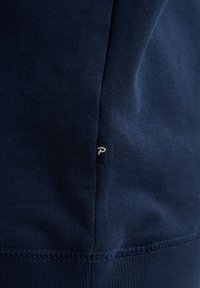 Tela de algodón azul marino, textura suave, diseño ajustado, con una pequeña etiqueta de logo en la costura lateral. Costuras cuidadas a lo largo de los bordes.