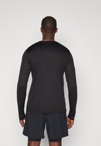 Sort langærmet skjorte lavet af glat stof, med rund halsudskæring og tætsiddende silhuet, parret med mørke shorts.