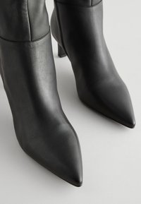Paire de bottines à bout pointu en cuir noir élégant avec fermetures éclair latérales et talons carrés sur un fond clair.