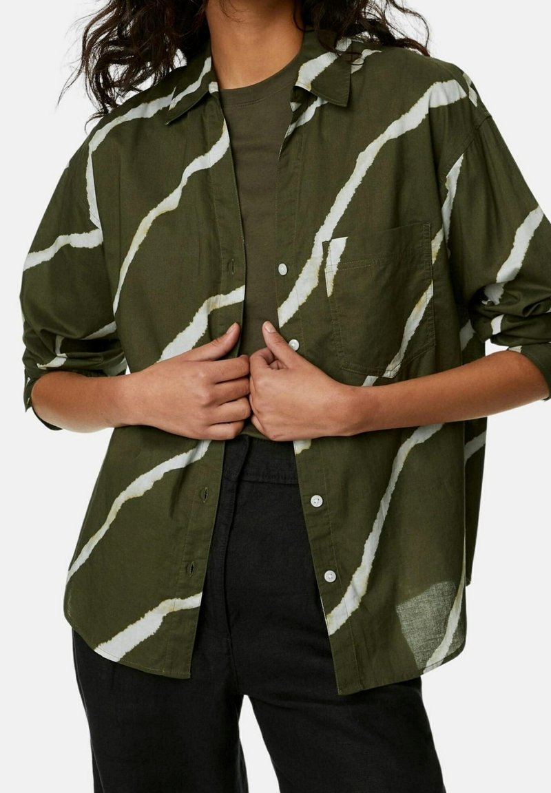Groene overhemd met knopen en een wit golvenpatroon, van textuurstof en met een borstzakje. Gecombineerd met een donkere top en zwarte broek.