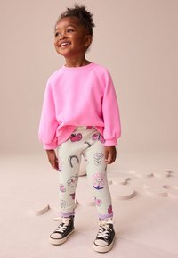 Felpa rosa con maniche a palloncino, leggings bianchi con motivo a fiori e arcobaleni, e sneakers alte nere.