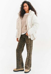 Kremowa pikowana kurtka, beżowy sweter z dzianiny i spodnie w panterkę. Strój cechuje się luźnym krojem i teksturowanymi materiałami.