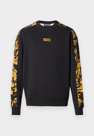 Black sweatshirt with long sleeves, featuring bold gold baroque patterns on sleeves and a central logo patch. Soft fabric texture.
