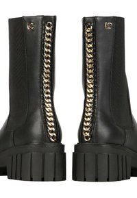 Botas negras hasta el tobillo con una suela de goma gruesa, que presentan un detalle de cadena dorada a lo largo del costado y paneles elásticos para facilitar el uso.