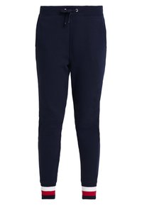 Mörkblå sweatpants i mjukt tyg, med dragsko i midjan och ribbade muddar med röda och vita ränder vid anklarna.