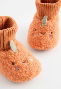 Orange, texturerade småbarns tofflor med ribbad stickad mudd. Har ett leende ansikte med broderade detaljer och en liten tygstam.