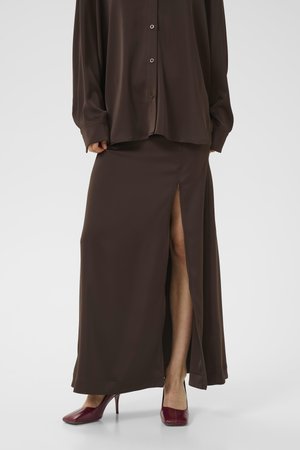 Woman wearing a dark brown long skirt with a front slit and matching button-up shirt, paired with burgundy high-heeled shoes.